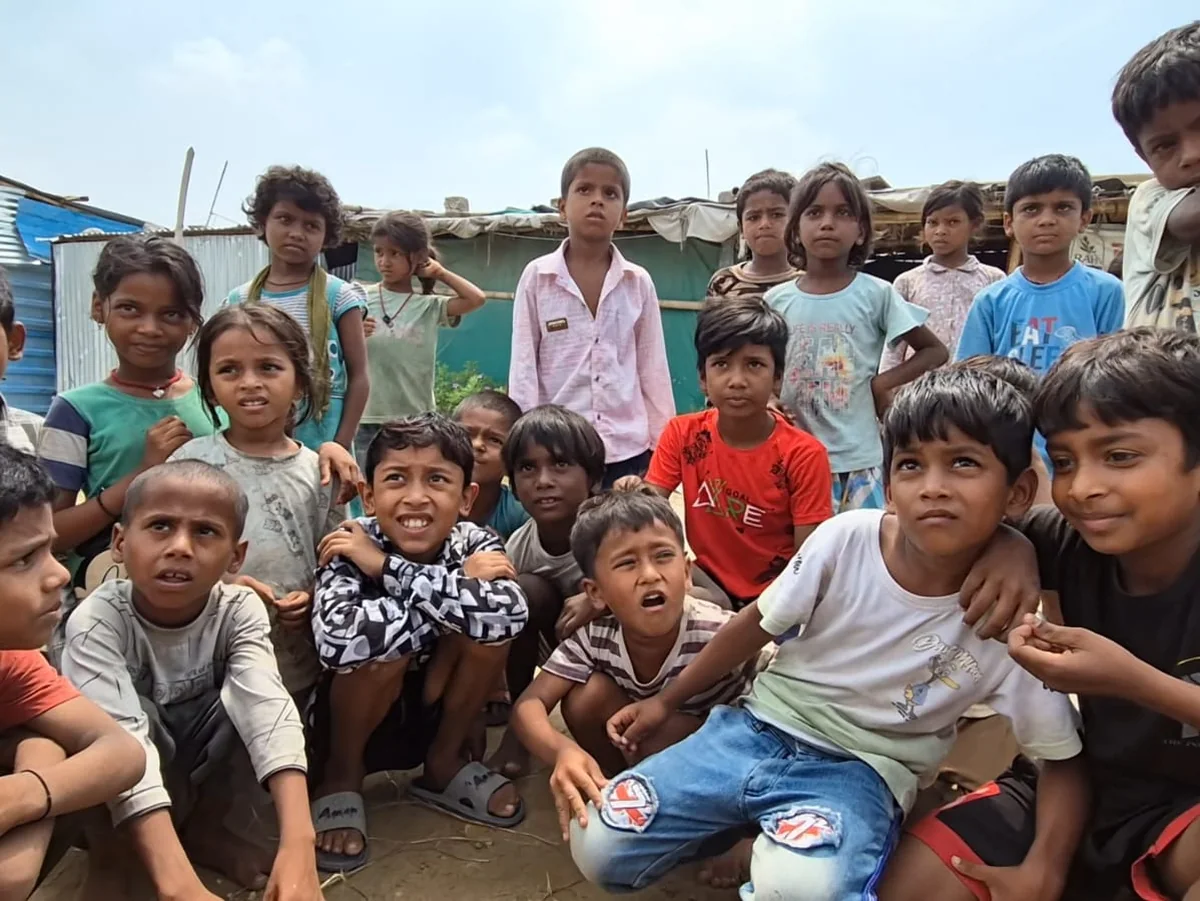 A large group of children gathered outside their homes in a settlement of corrugated-metal shelters.